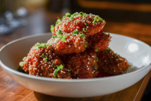 A bowl of bright orange Redd Wings with a Thai chili glaze, sprinkled with sesame seeds and chives at Redd Rochester 