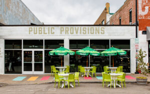 View of the front of Public Provisions at the Rochester Public Market with outdoor tables and umbrellas on the sidewalk and street