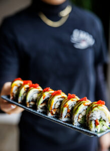 A server carries a platter with a sliced Dragon roll at Umai Revolving Sushi in Rochester NY