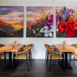 The dining room at Wildflour restaurant in Rochester NY with wooden tables and chairs and large floral paintings on the wall