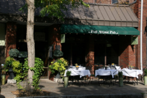 View of the front entrance to Park Avenue Pub in Rochester NY with sidewalk tables and green awning