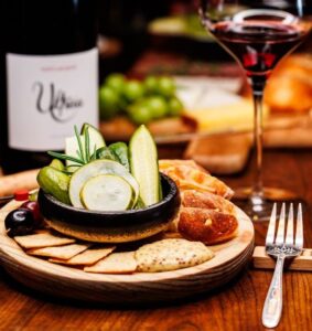 The pickle plate with assorted pickled veggies, fruit, mustard, and crackers, with a glass and bottle of red wine at Pintxo Wine Bar in Canandaigua NY