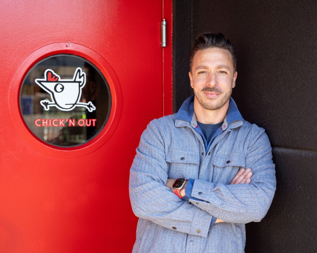 Adam Bierton, the owner of Chick'n Out restaurant in Rochester NY, poses next to its bright red door