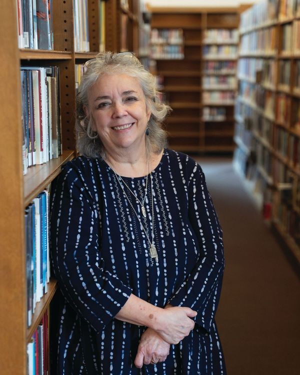 Patty Uttaro, director of the Monroe County Library System (MCLS) and the Rochester Public Library (RPL), gently leans against a bookshelf while smiling in the Rochester Public Library in Rochester, N.Y.