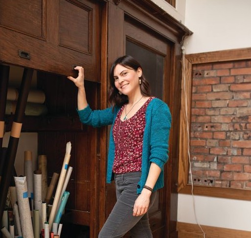 Rachael Gootnick, founder of Just Terrific HandCrafted Goods - specializing in book repairs and restorations, stands in front of open compartment in wall with supplies in Rochester, N.Y.