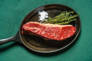 A piece of raw steak with rosemary and sea salt on a cast iron pan at Patron Saint steakhouse in Rochester NY