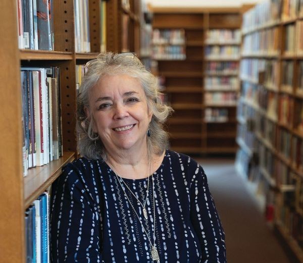 Patty Uttaro, director of the Monroe County Library System (MCLS) and the Rochester Public Library (RPL), gently leans against a bookshelf while smiling in the Rochester Public Library in Rochester, N.Y.