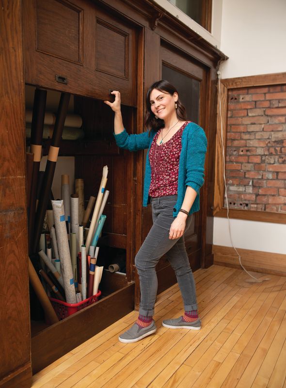 Rachael Gootnick, founder of Just Terrific HandCrafted Goods - specializing in book repairs and restorations, stands in front of open compartment in wall with supplies in Rochester, N.Y.