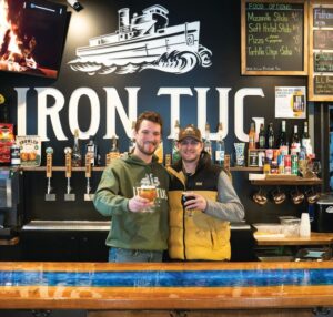 Zach Allard, head brewer, and Mike Nulton, current owner of Iron Tug Brewing posing behind bar in Rochester, N.Y.