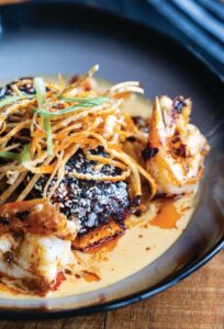 Slammin’ Salmon with grilled shrimp, spicy coconut broth, stir-fried vegetables, fried rice crunchies, wonton strips, unagi glaze, and chili oil at Nosh in Rochester, N.Y.