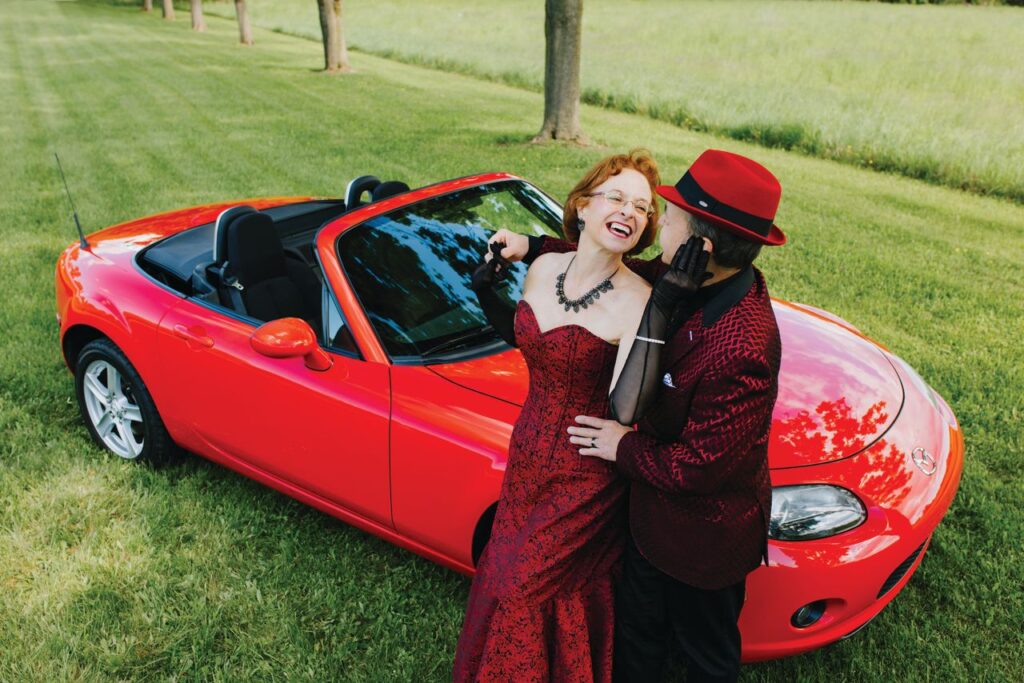 Dave and Sandra Sluberski posing and leaning on the hood of a red 2008 Mazda Miata in Rochester, N.Y.