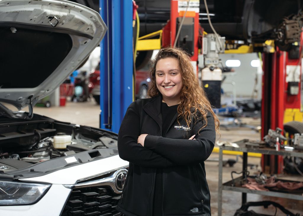 Kyla Paradiso, service advisor at Toyota of Rochester, posing in front of a white Toyota Highlander with the hood up in the Toyota of Rochester's service center.