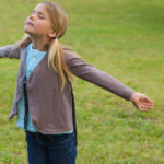 Young girl with arms outstretched and eyes closed at the park