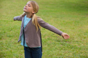 Young girl with arms outstretched and eyes closed at the park